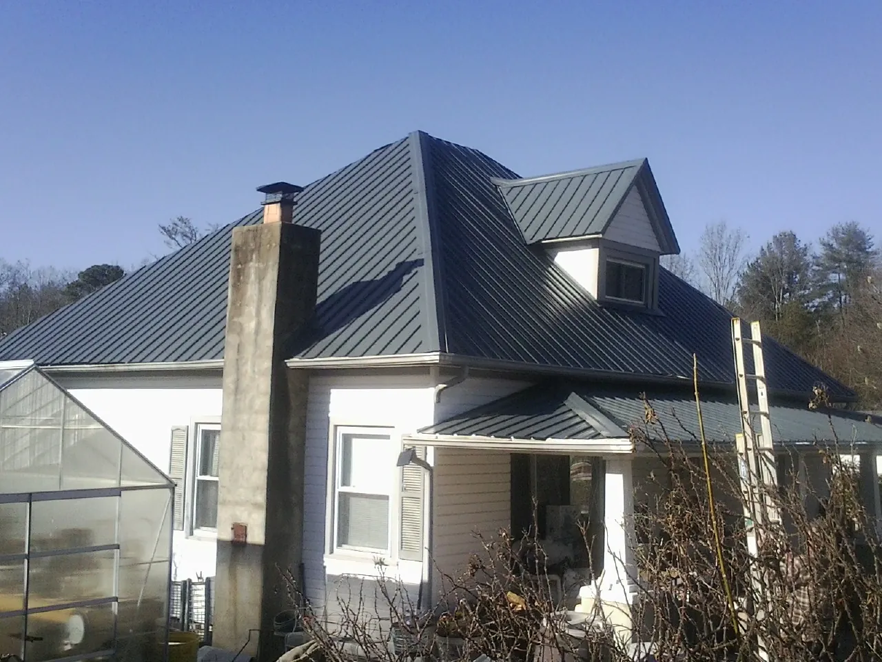 Dark blue standing seam metal roof on a white farmhouse with dormer — Slate & Tile Roof Repair by Roofing Brothers in Central Falls