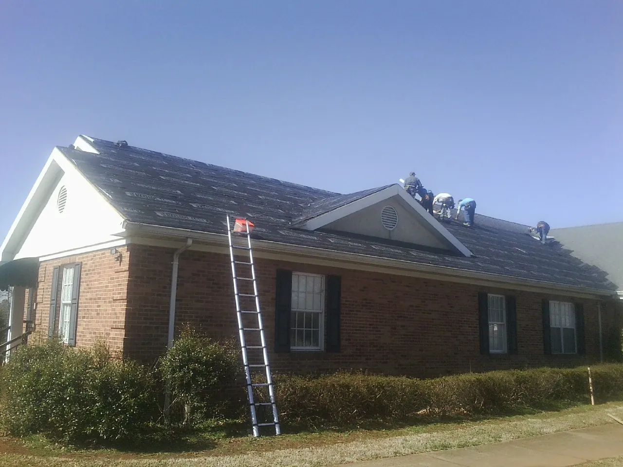 Crew tearing shingles off a brick ranch roof with a ladder set — Emergency Roof Repair work by our crew in Central Falls