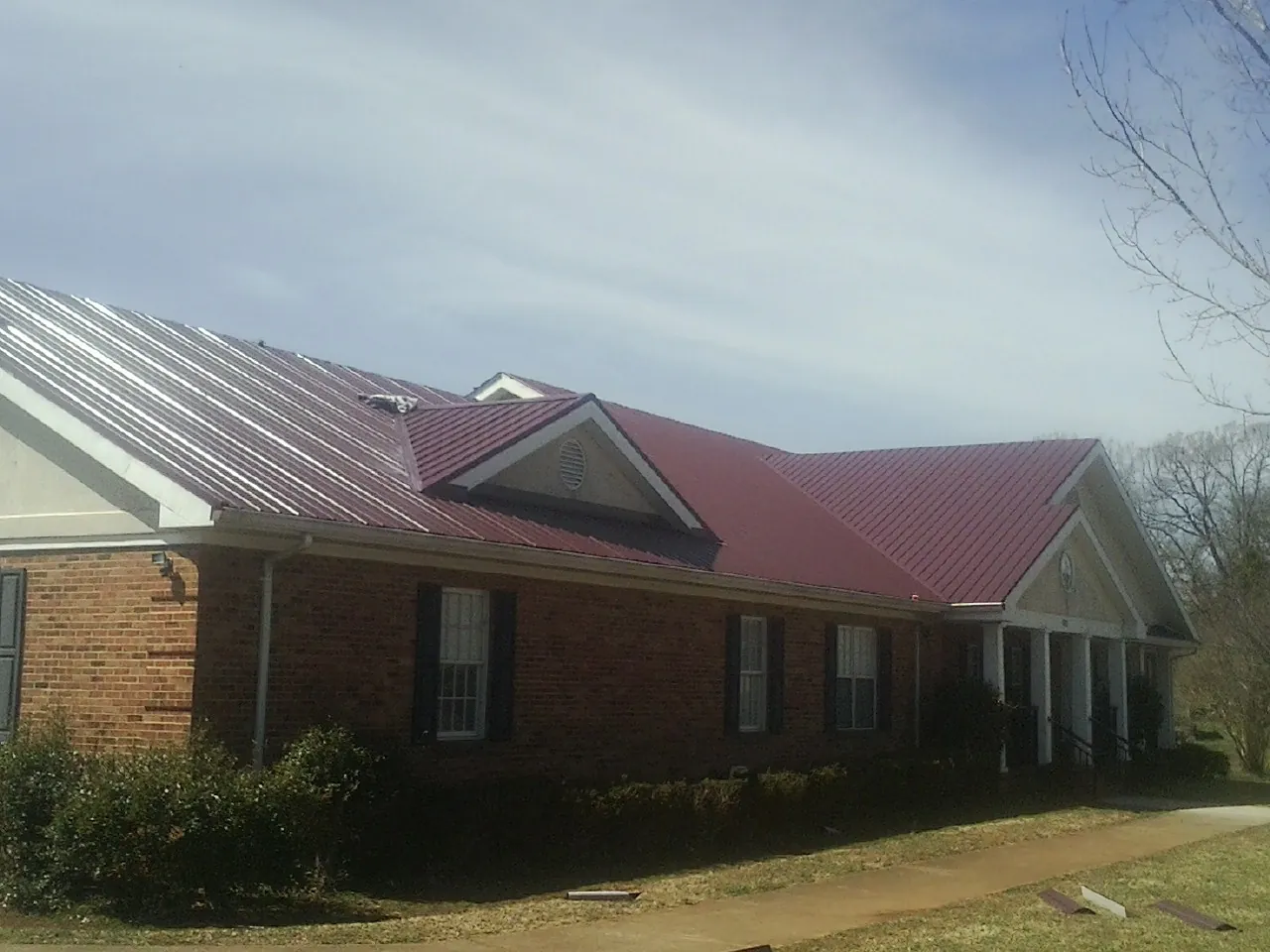 Red metal roof with gabled entries on a long brick building, from a Hail Damage Roof Repair job in Central Falls