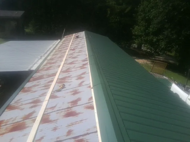 Old rusted panels beside newly installed green metal roofing — Wind Damage Roof Repair by Roofing Brothers in Central Falls