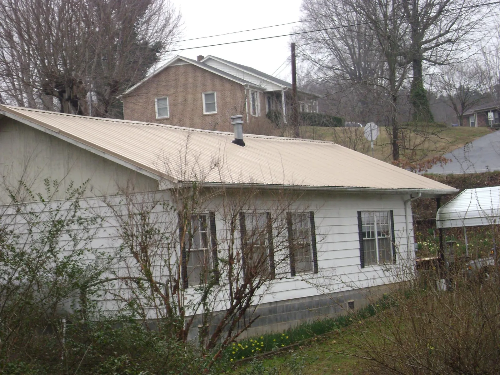 Tan metal roof on a white sided house set into a hillside — Commercial Roofing by Roofing Brothers in Central Falls